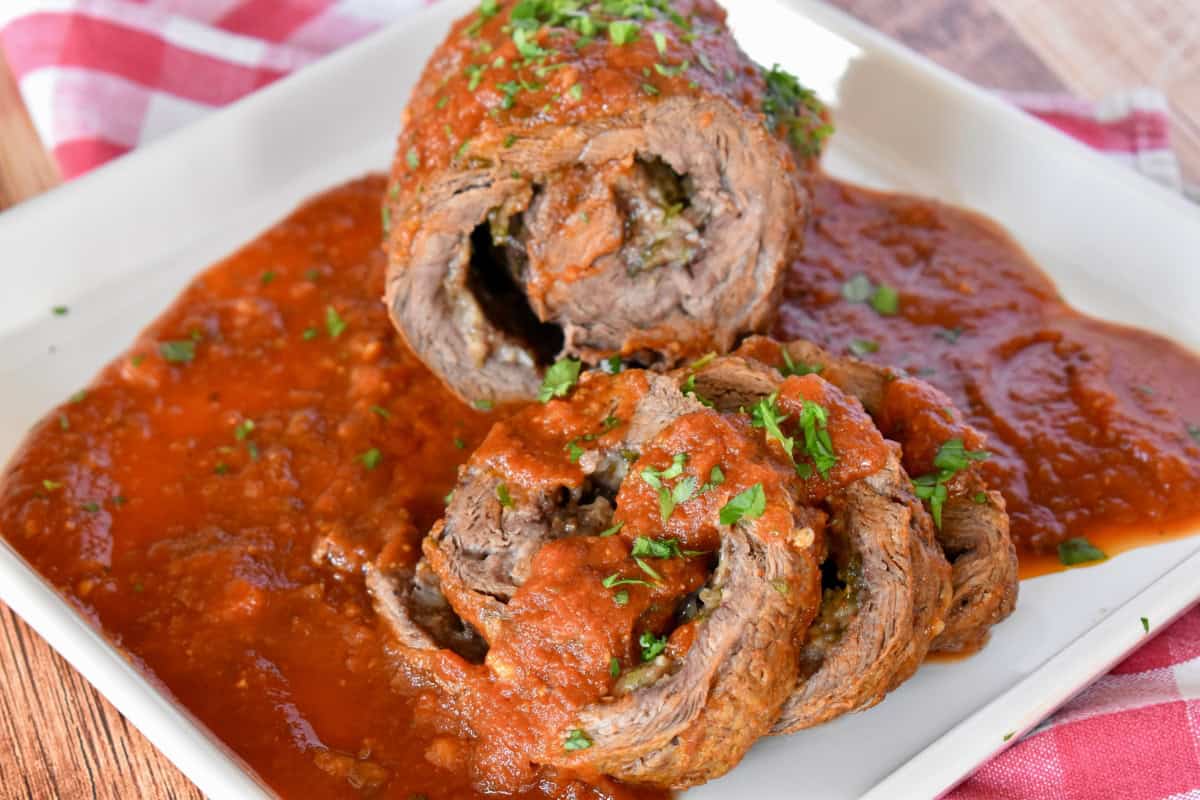 Slices of authentic Italian braciole on a white plate with marinara sauce on top. 