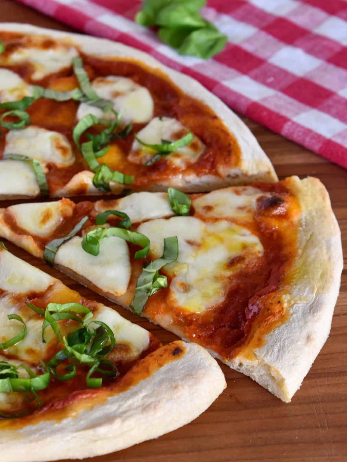 Italian Margherita Pizza slice on a cutting board with checkered napkin.