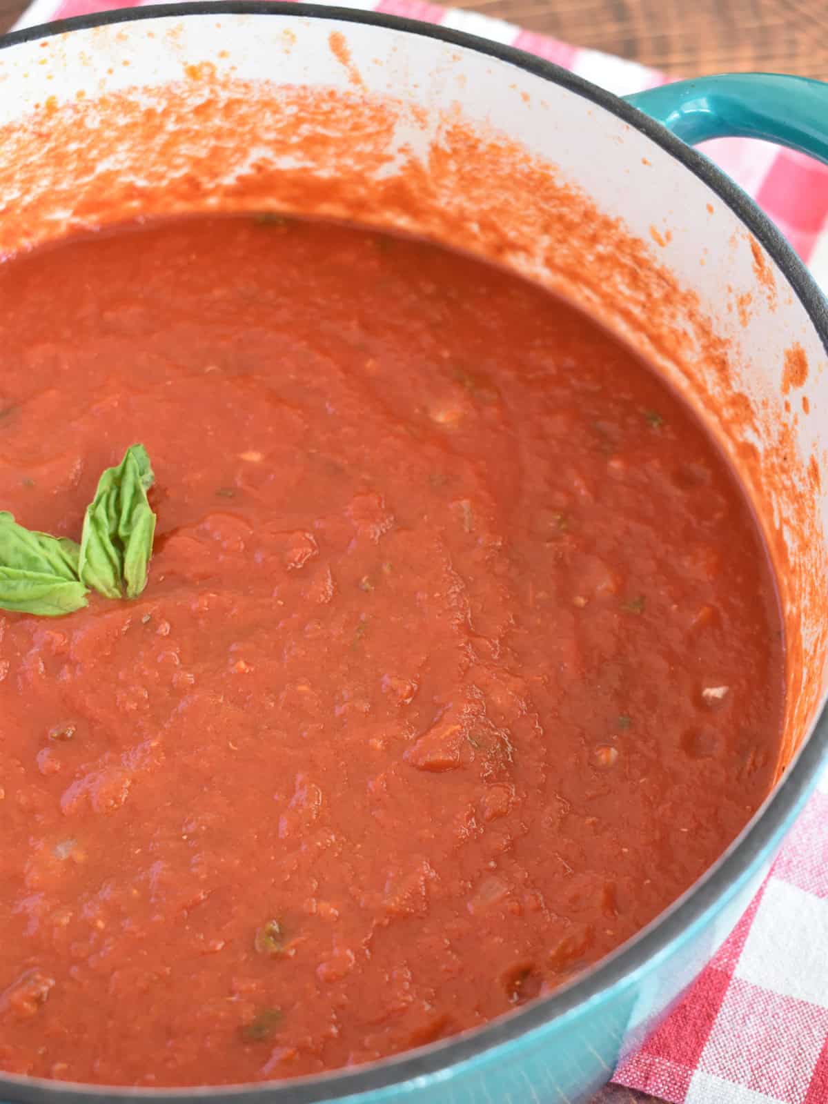 Marinara sauce that has not been blended in a dutch oven with basil leaves on top. 