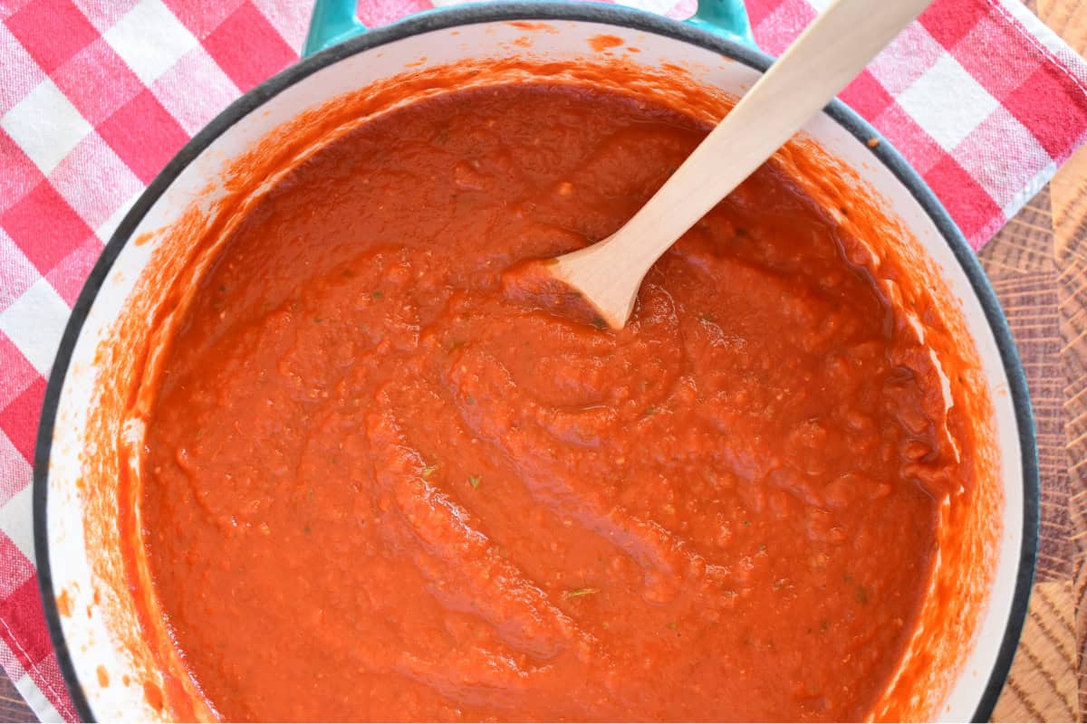 Simple marinara sauce in a dutch oven with a spoon. 