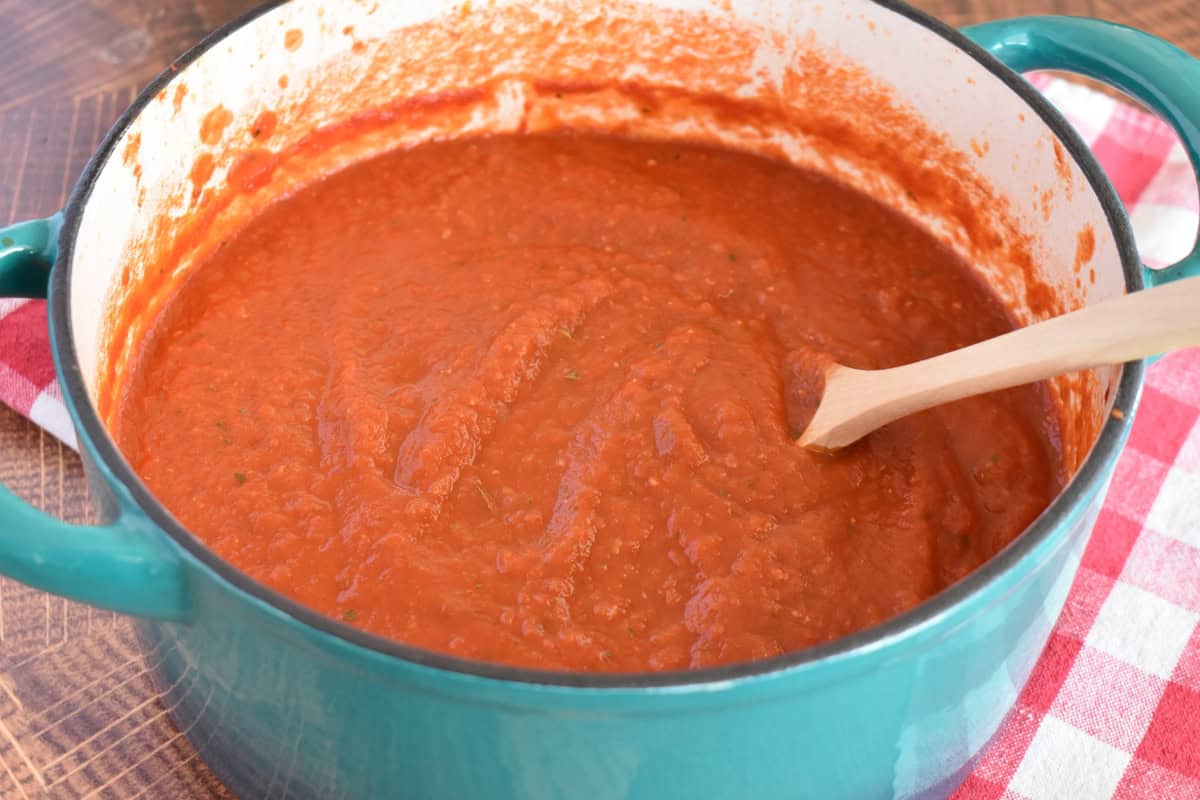 Simple marinara sauce in a dutch oven with a wooden spoon. 