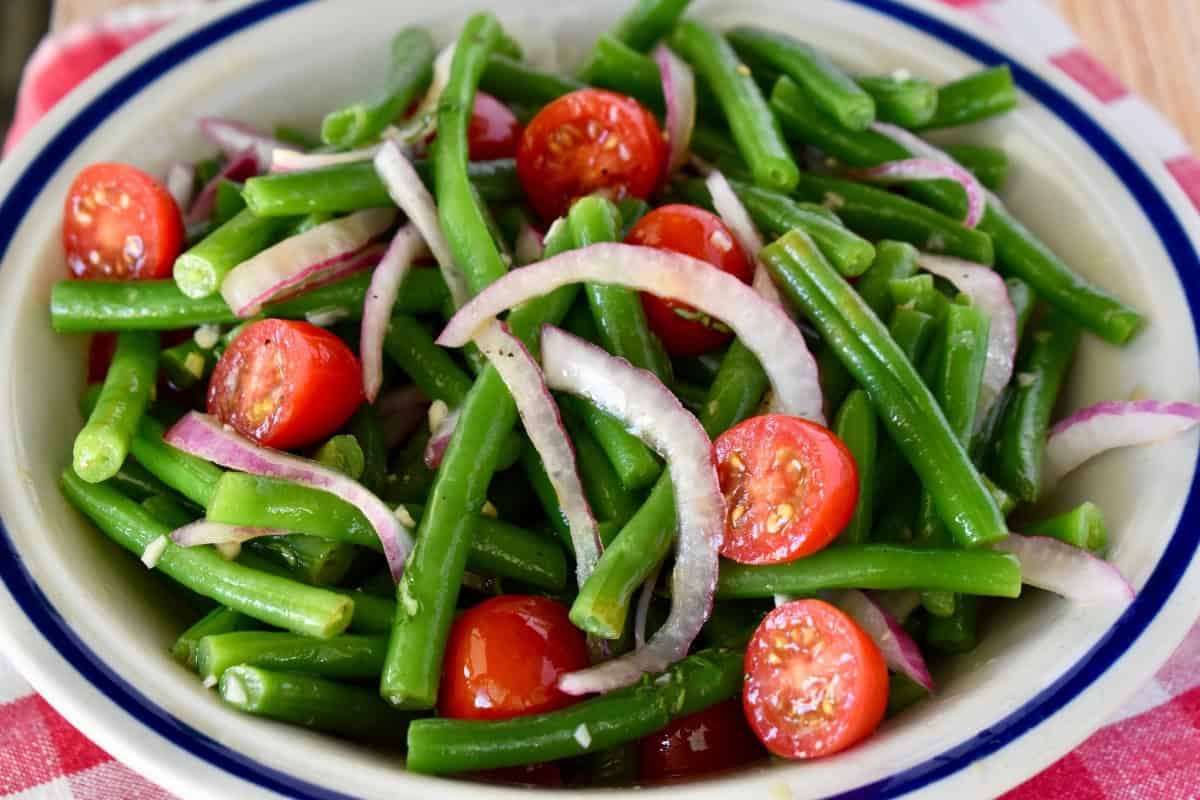A bowl of green beans and tomatoes with onions.