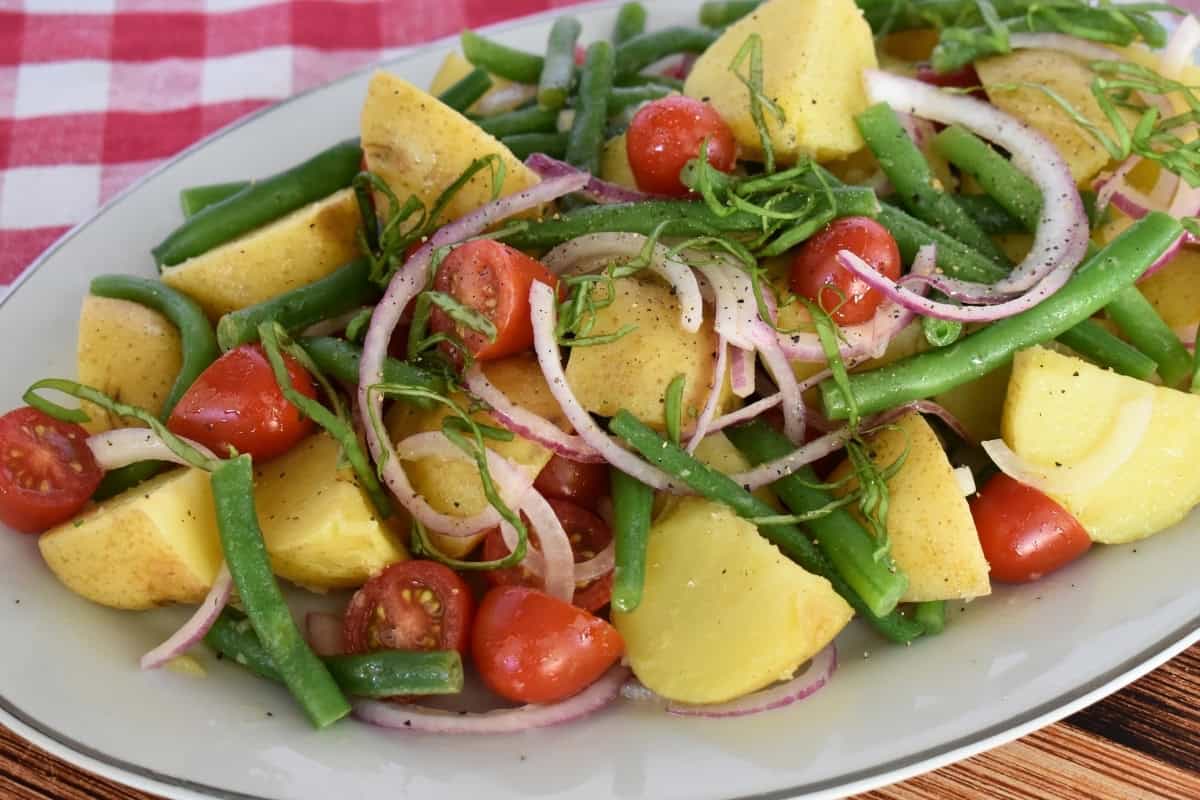 Italian Potato salad in a white bowl with a checkered napkin underneath. 
