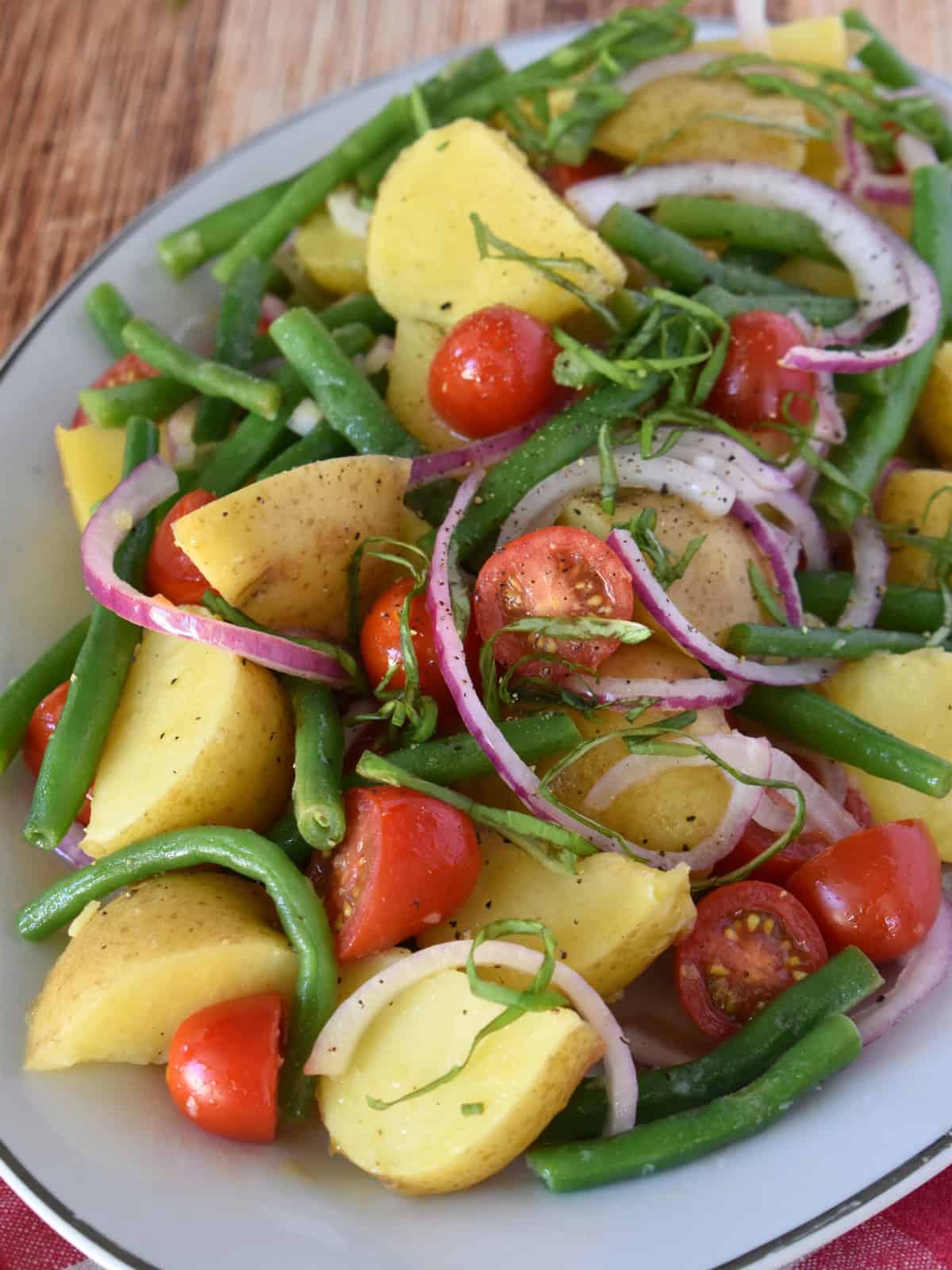 Italian Potato Salad in a white bowl with red onions on top.