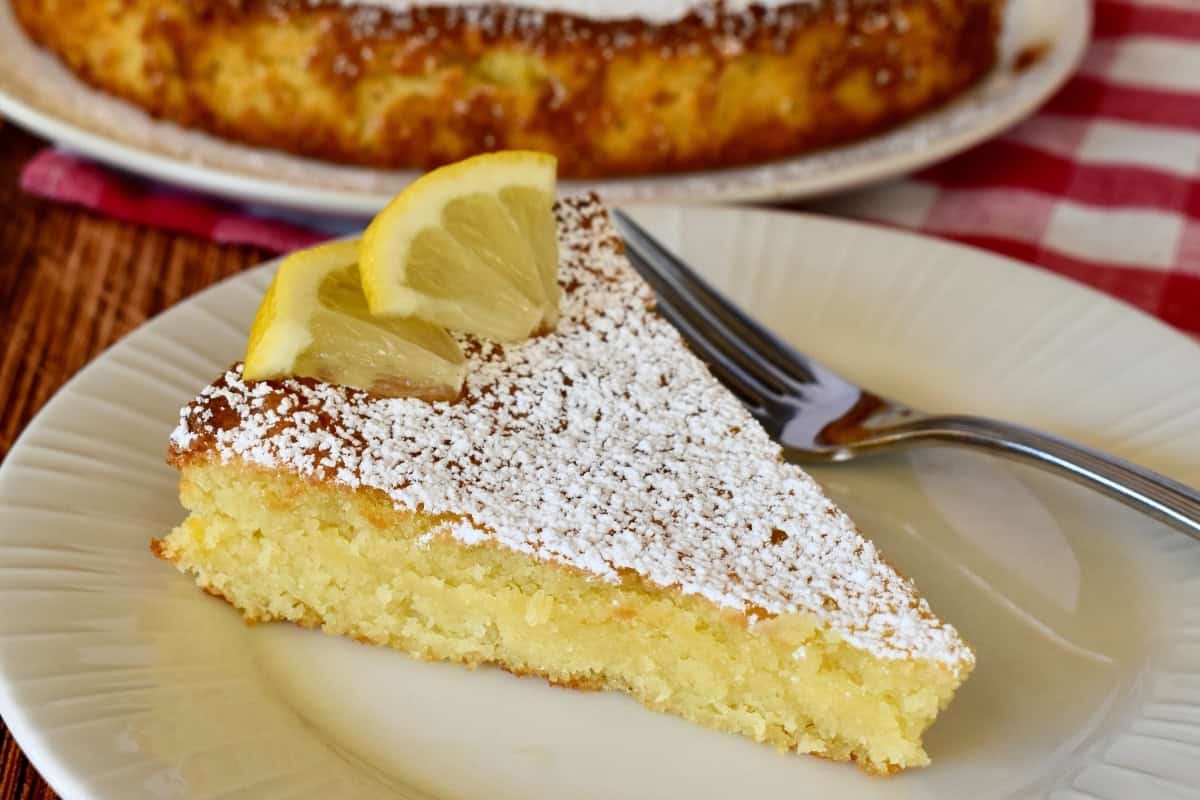 Slice of lemon torta caprese with lemon slices on top on a white plate.