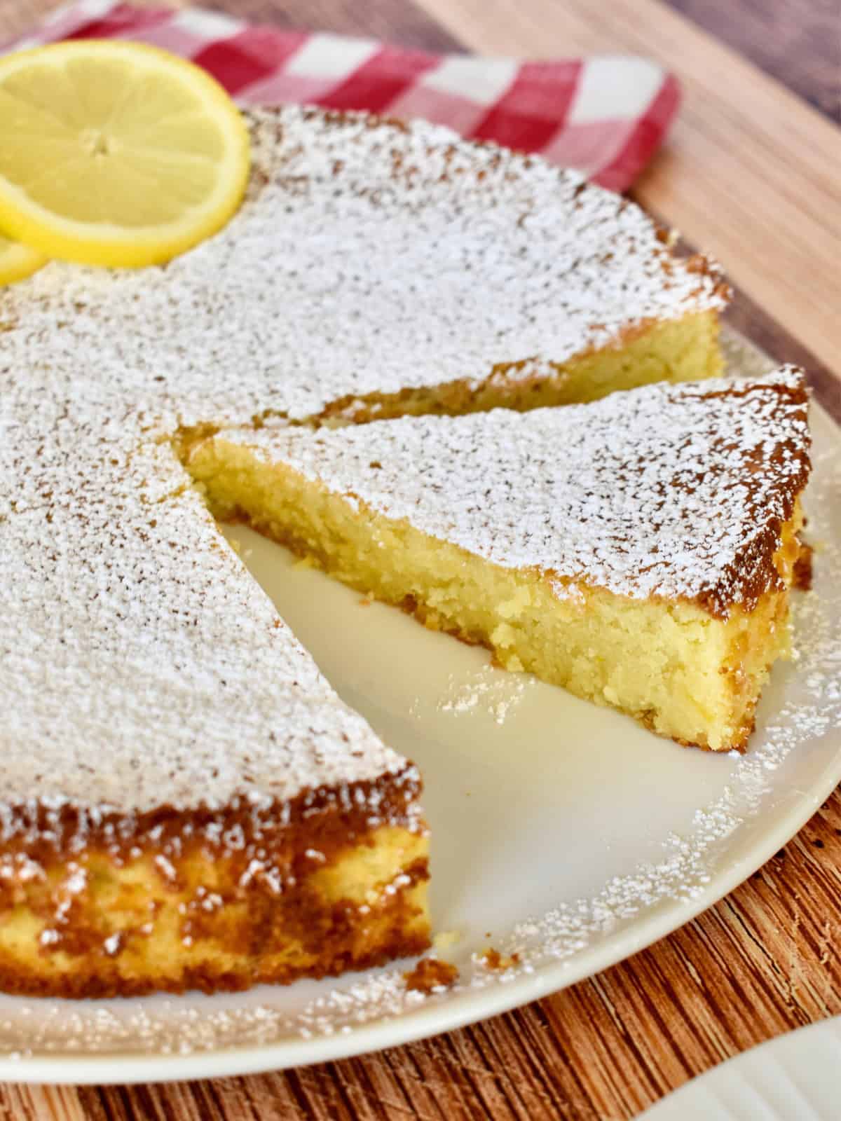 A lemon torta caprese cake with lemon slices on top and a slice missing.