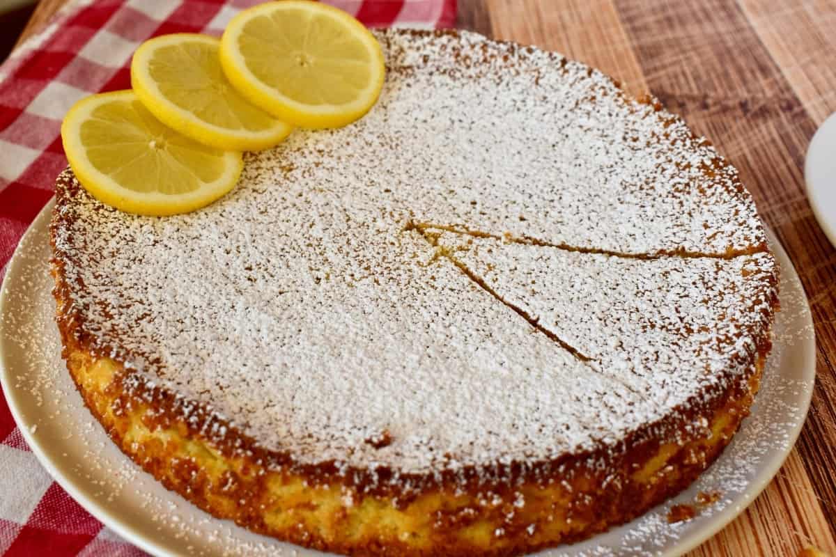 Lemon torta caprese with powdered sugar sprinkled on top and sliced lemon.