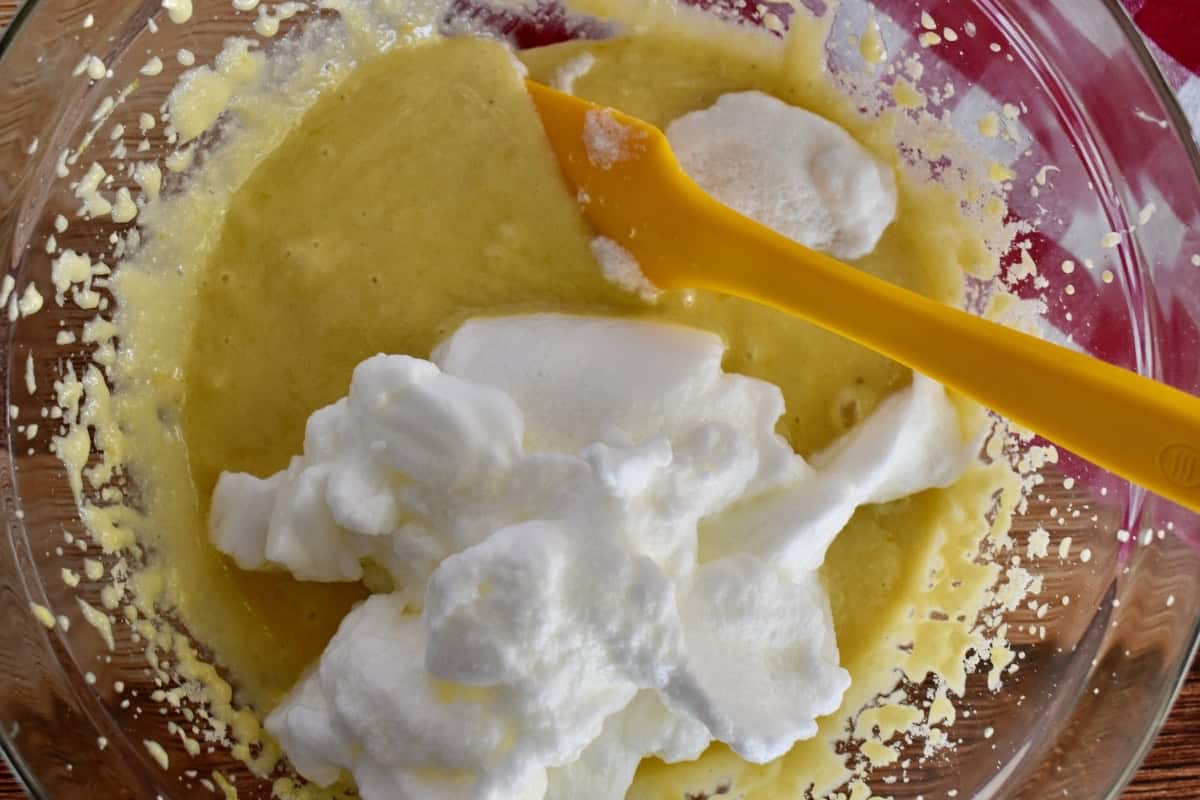 Egg whites on top of the cake batter with a rubber spatula in a glass bowl.