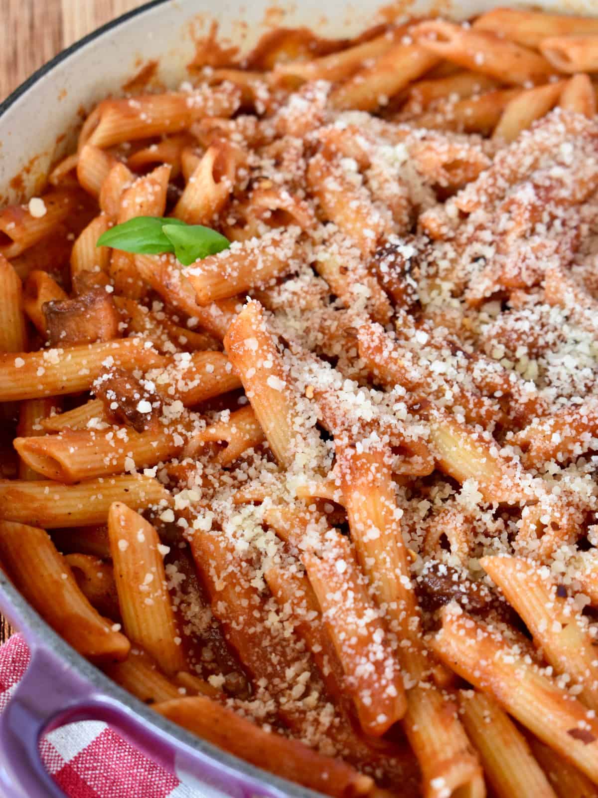 Penne all'Amatriciana in a large pot with grated cheese and a basil leave on top. 