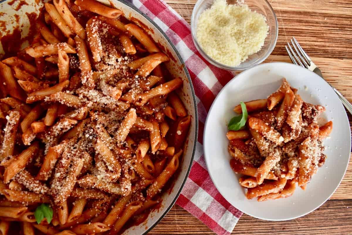 Penne all'Amatriciana in a large pot with a plate next to it and some grated parmesan cheese. 
