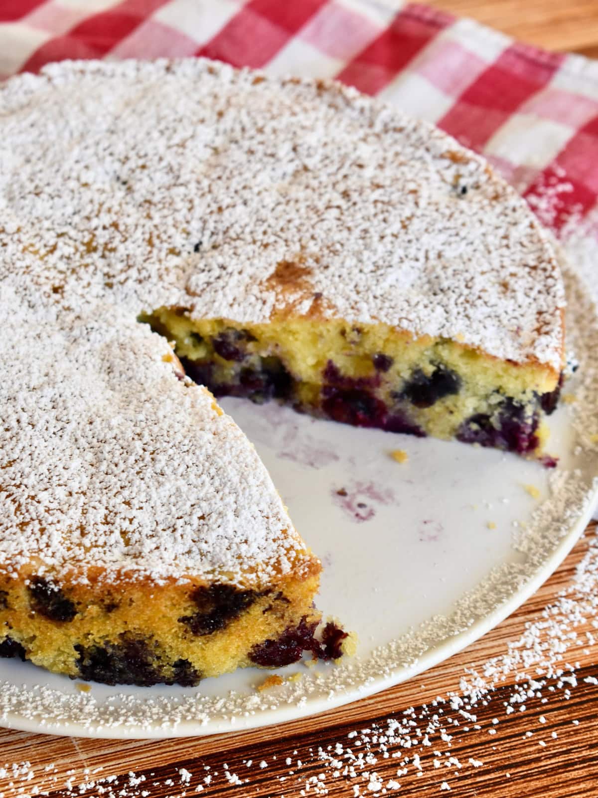 Blueberry polenta cake with a slice cut from it and powdered sugar sprinkled on top.