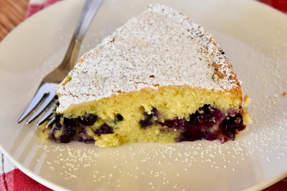 Slice of blueberry polenta cake on a white plate with a fork. 