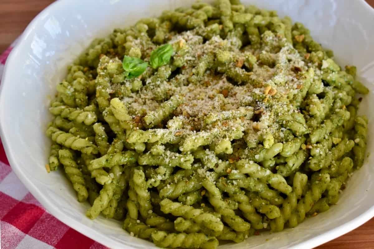 Pistachio pesto tossed with pasta in a large white bowl. 