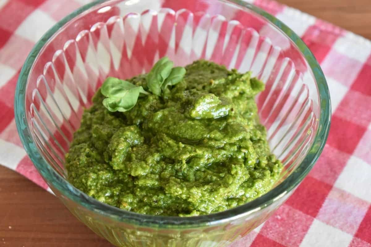 Pistachio pesto in a glass bowl with checkered napkin behind it. 