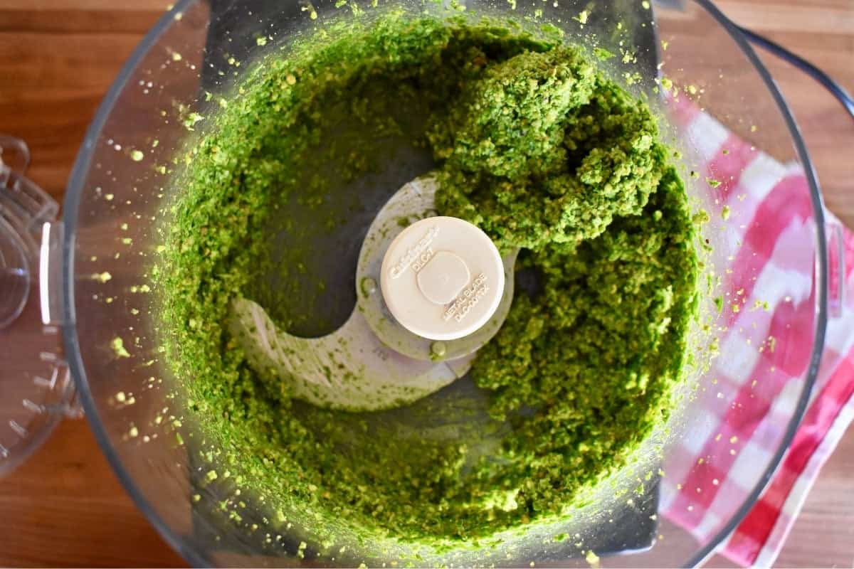 Ingredients including basil processed in a food processor. 