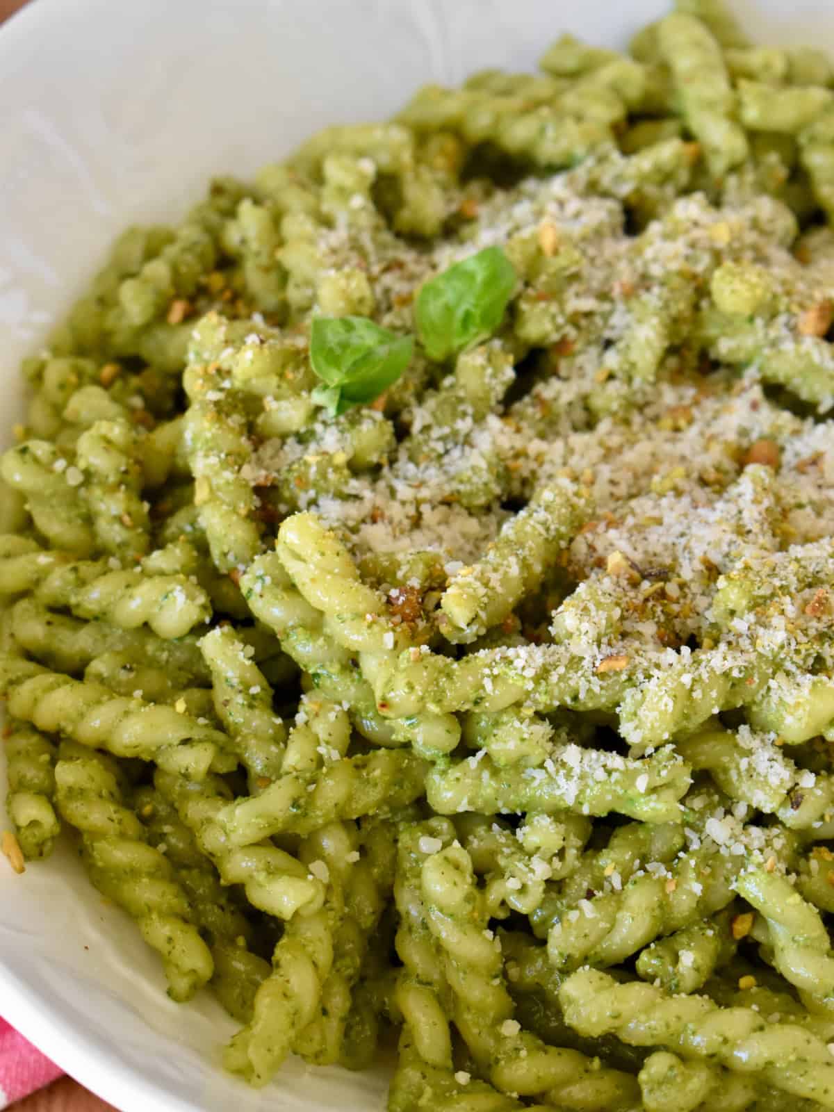 Pistachio pesto tossed with hot pasta in a white serving bowl. 