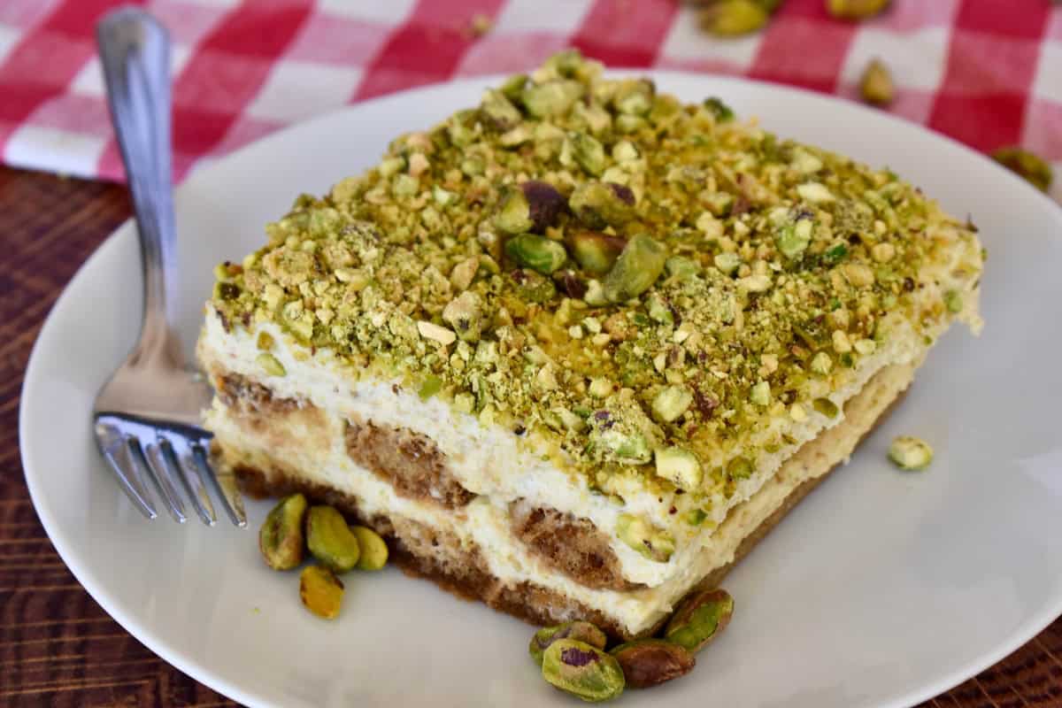 Pistachio Tiramisu with pistachios on top on a white plate with a checkered napkin. 