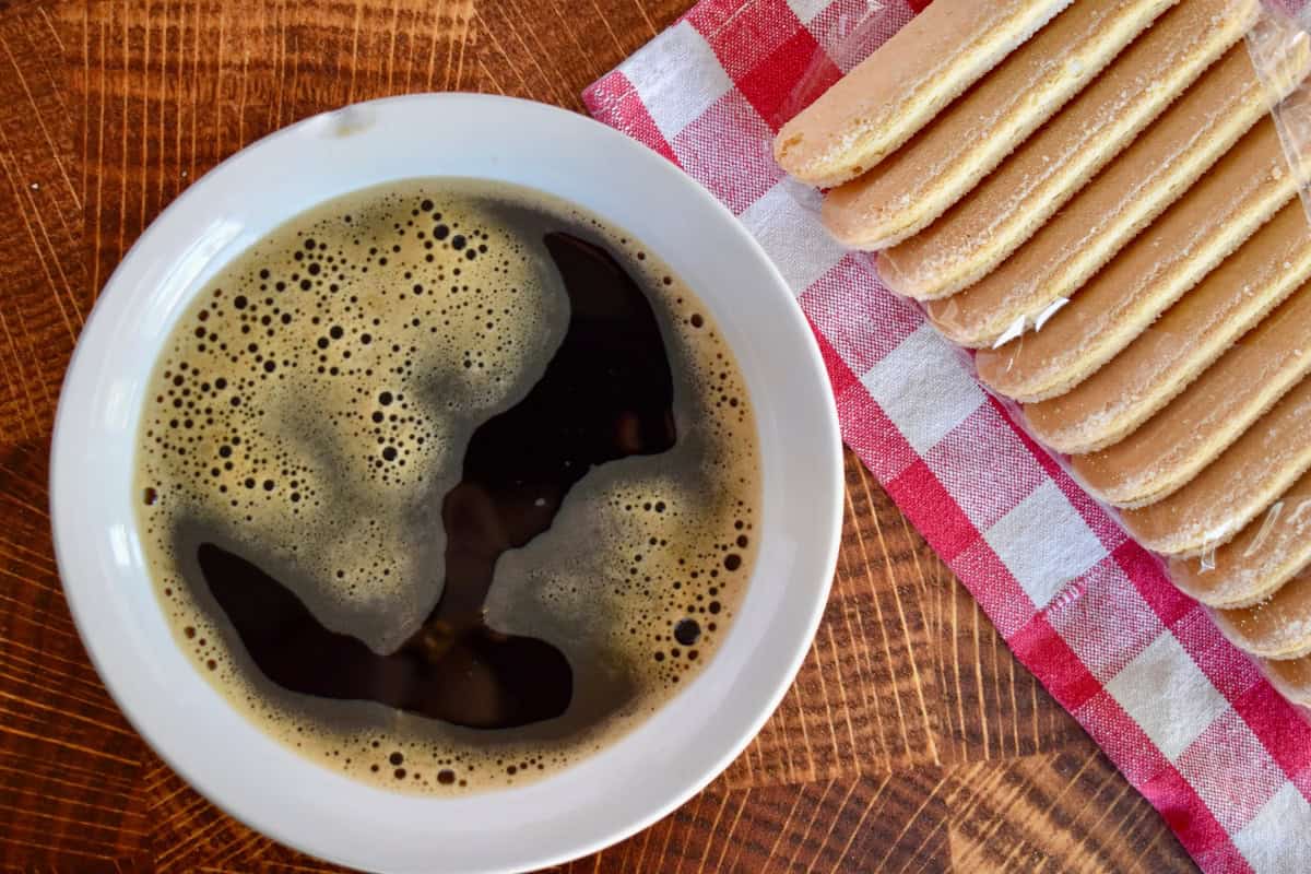 Strong coffee in a white bowl with ladyfingers next to it. 