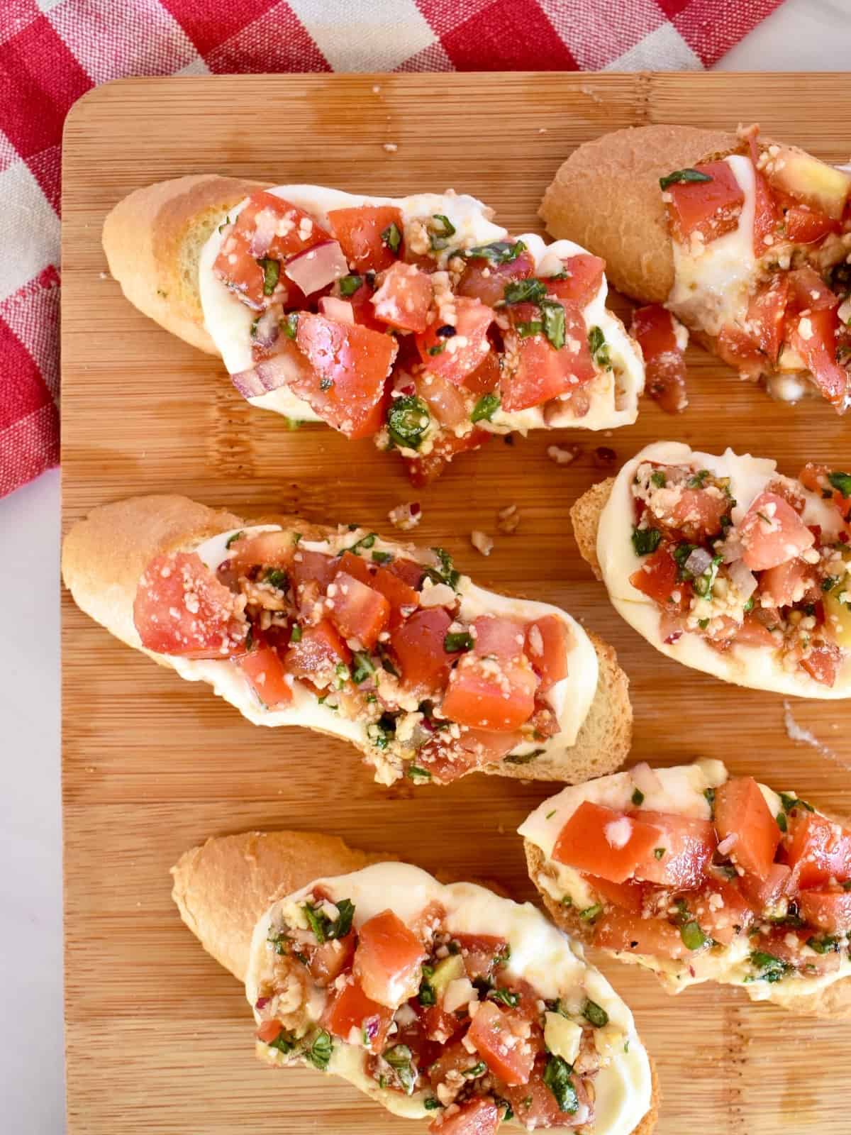 Toasted bread topped with ricotta and diced tomatoes on a wood board. 