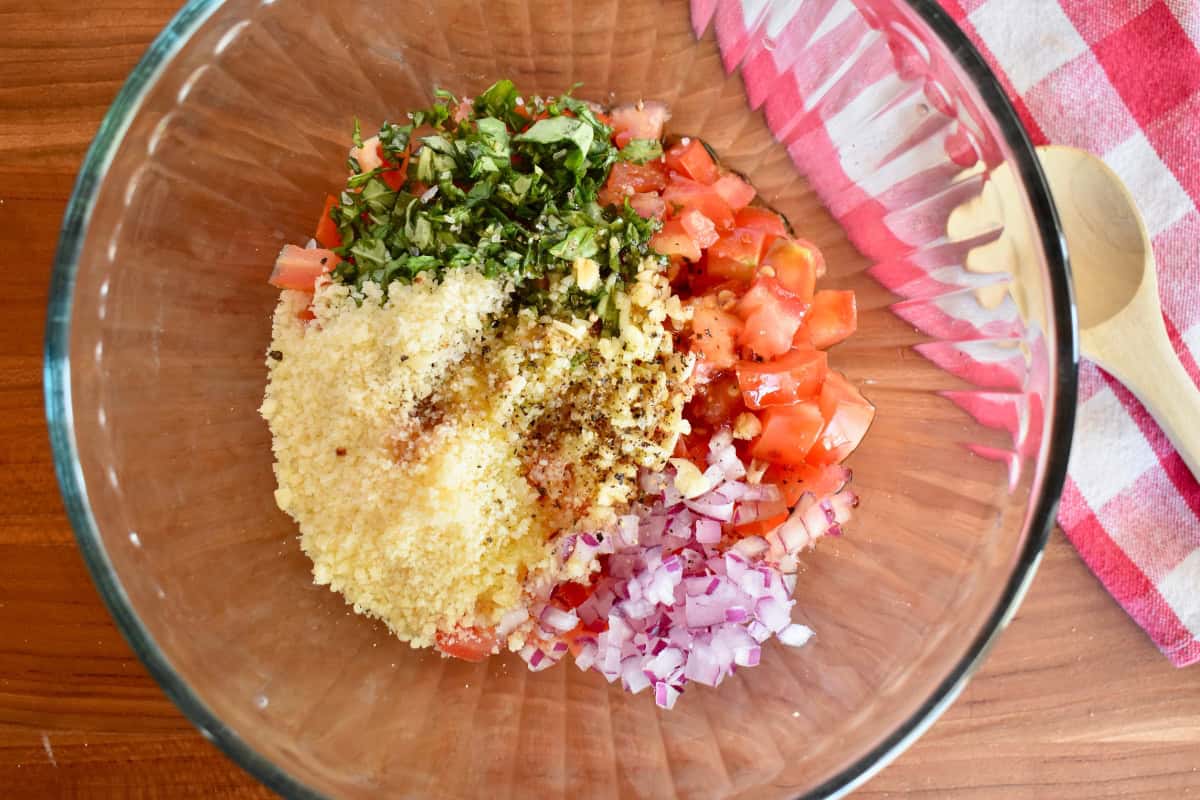 Diced tomatoes, basil, onions, garlic, olive oil, balsamic, and onions in a glass bowl. 