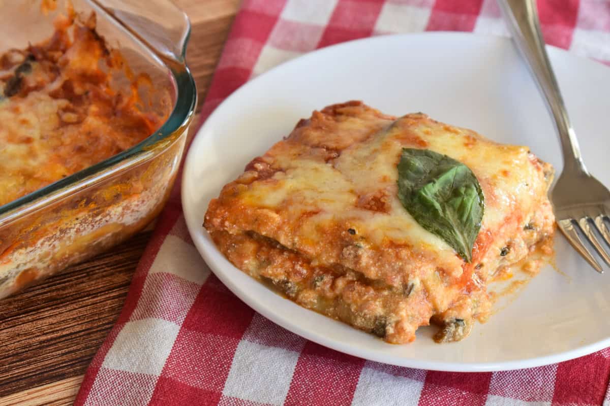 Slice of eggplant lasagna on a white plate with a fork. 