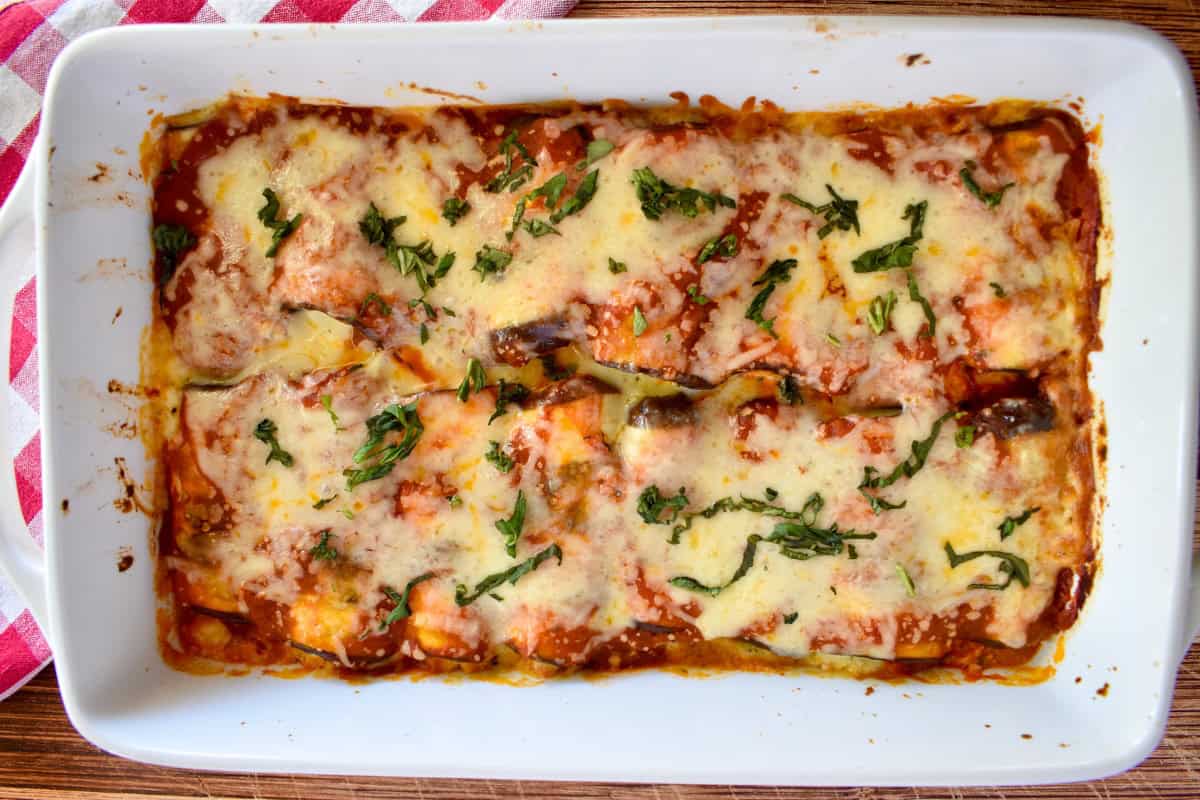 Eggplant Rollatini in a white baking dish with melted cheese and basil on top. 