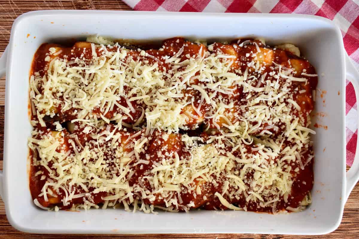 Eggplant rollatini in a white baking dish with shredded mozzarella cheese sprinkled on top. 