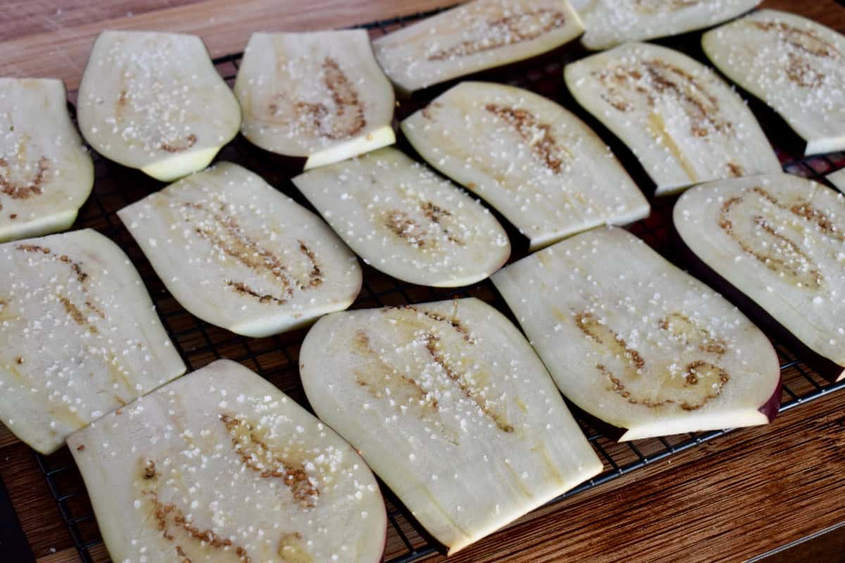 Slices of eggplant on a wire rack with salt sprinkled on top. 