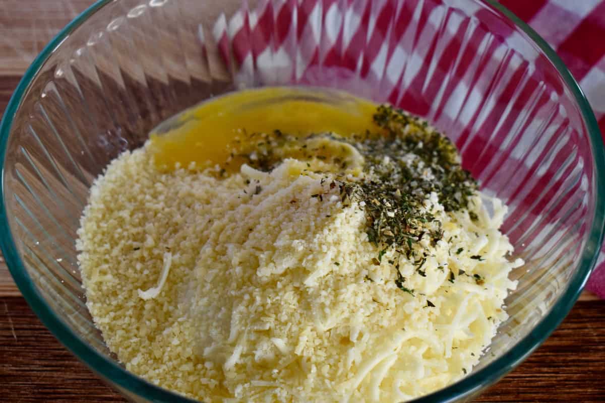 Ingredients for filling in a glass bowl including ricotta, cheese, egg, and parsley. 