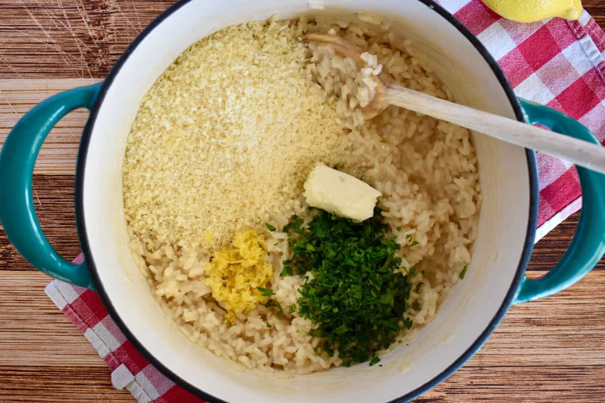 Cooked arborio rice, butter, and parsley in a large dutch oven with a wooden spoon. 
