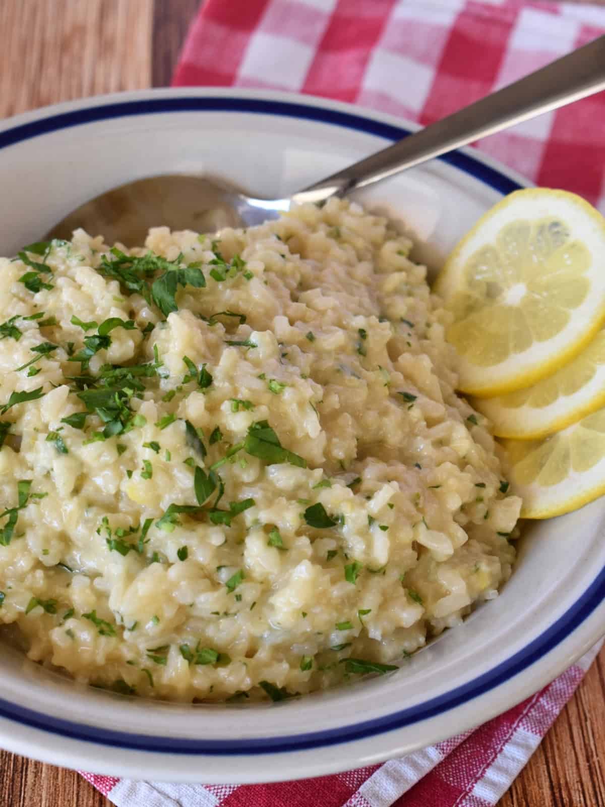 Lemon Risotto in a white bowl with a spoon on a checkered napkin. 