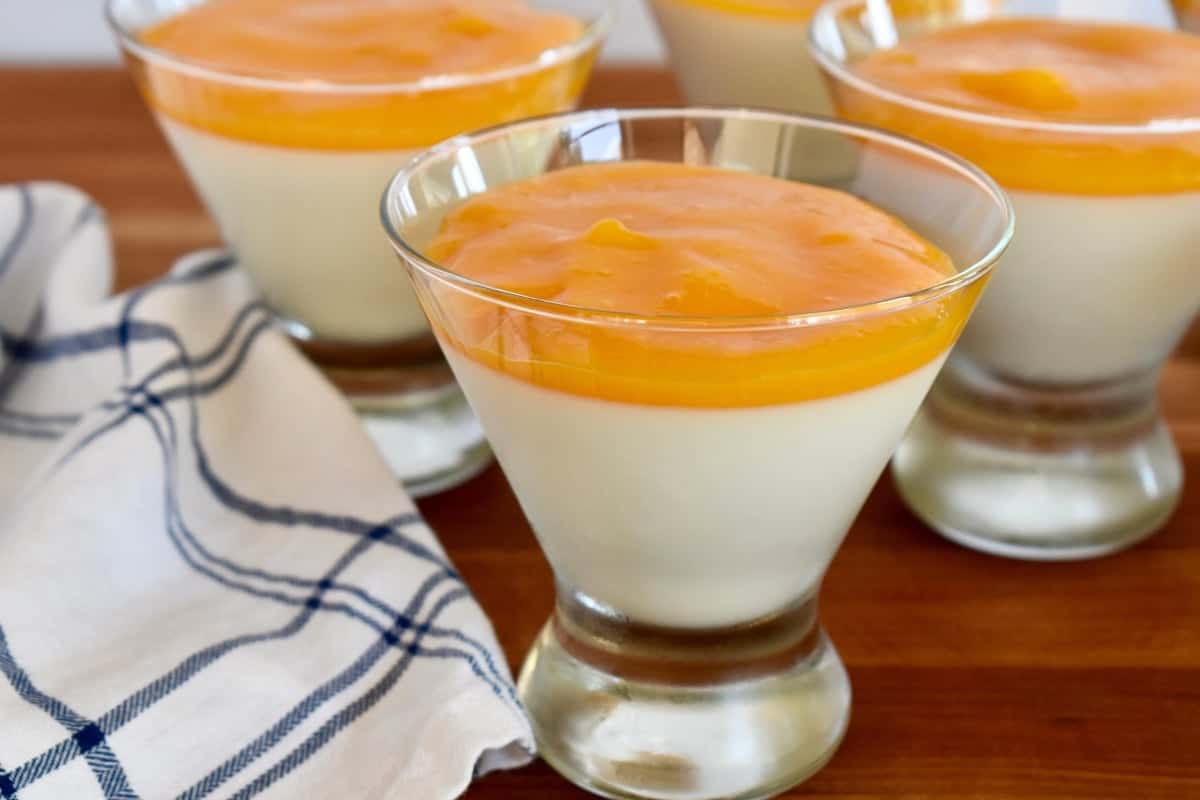 Mango Panna Cotta in a glass on a wood cutting board. 