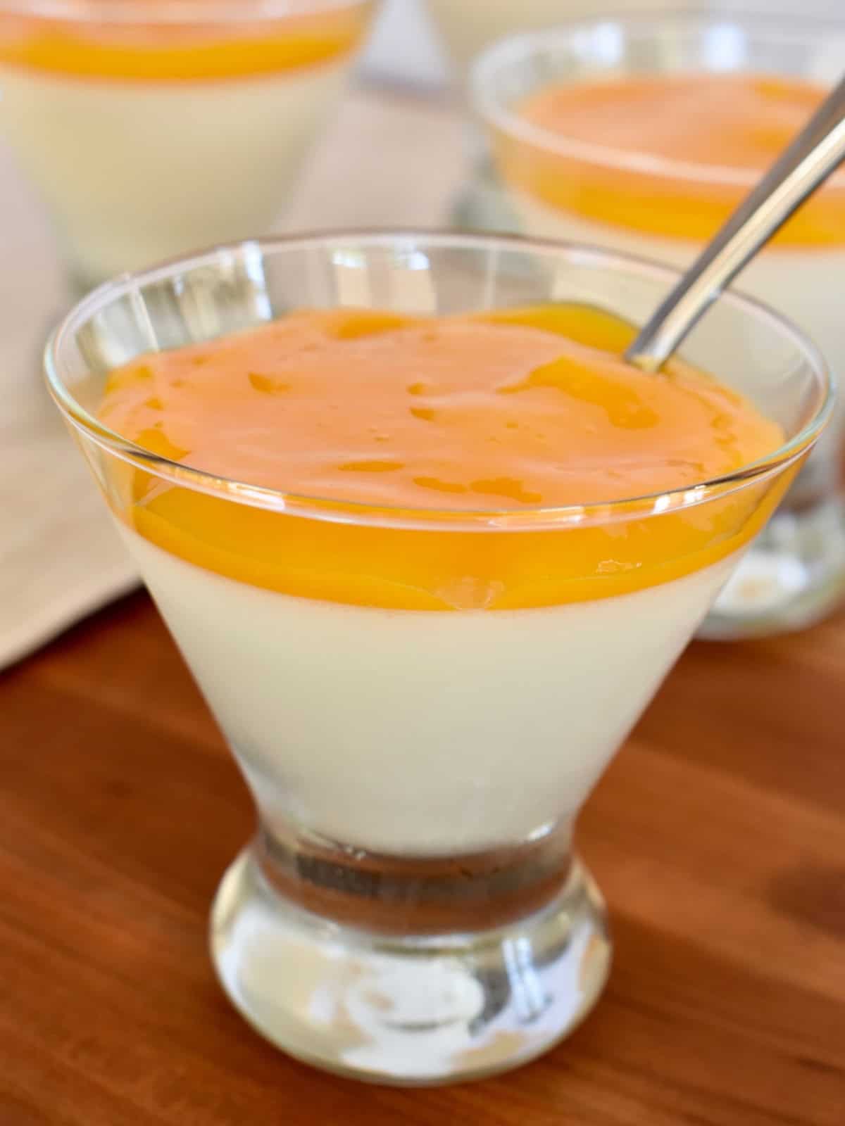 Mango panna cotta in a glass cup with a spoon. 