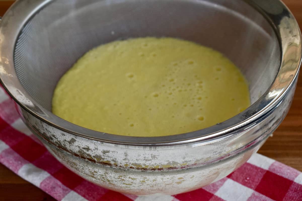 Egg mixture being strained through a fine mesh sieve into a bowl. 