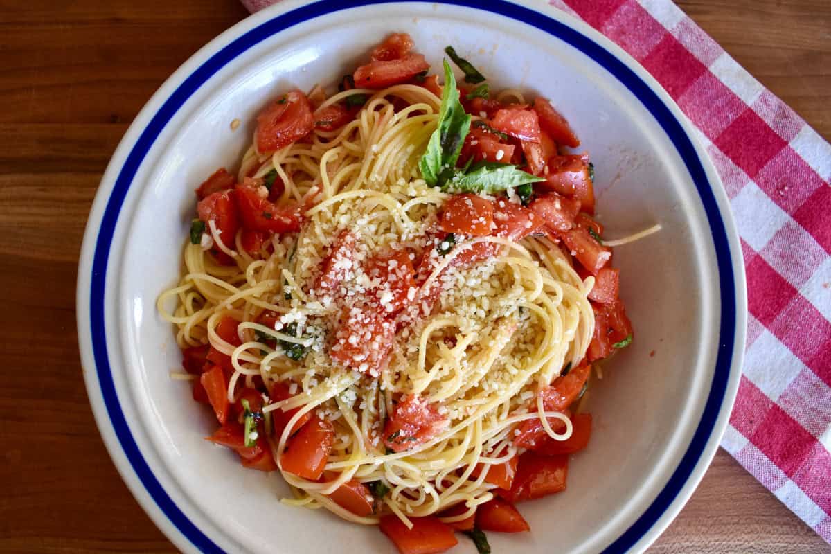 Raw tomato sauce tossed with angel hair pasta in a bowl. 