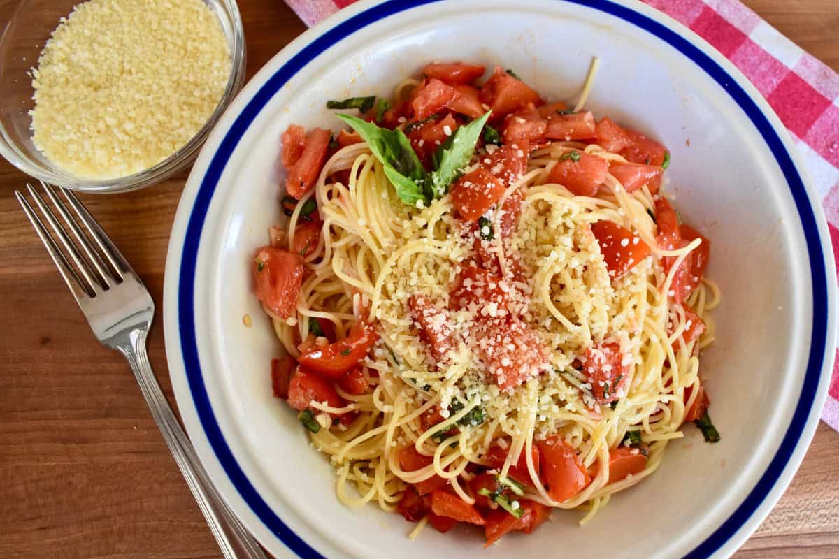 Recipe in a white bowl with a bowl of parmesan cheese and a fork next to it. 