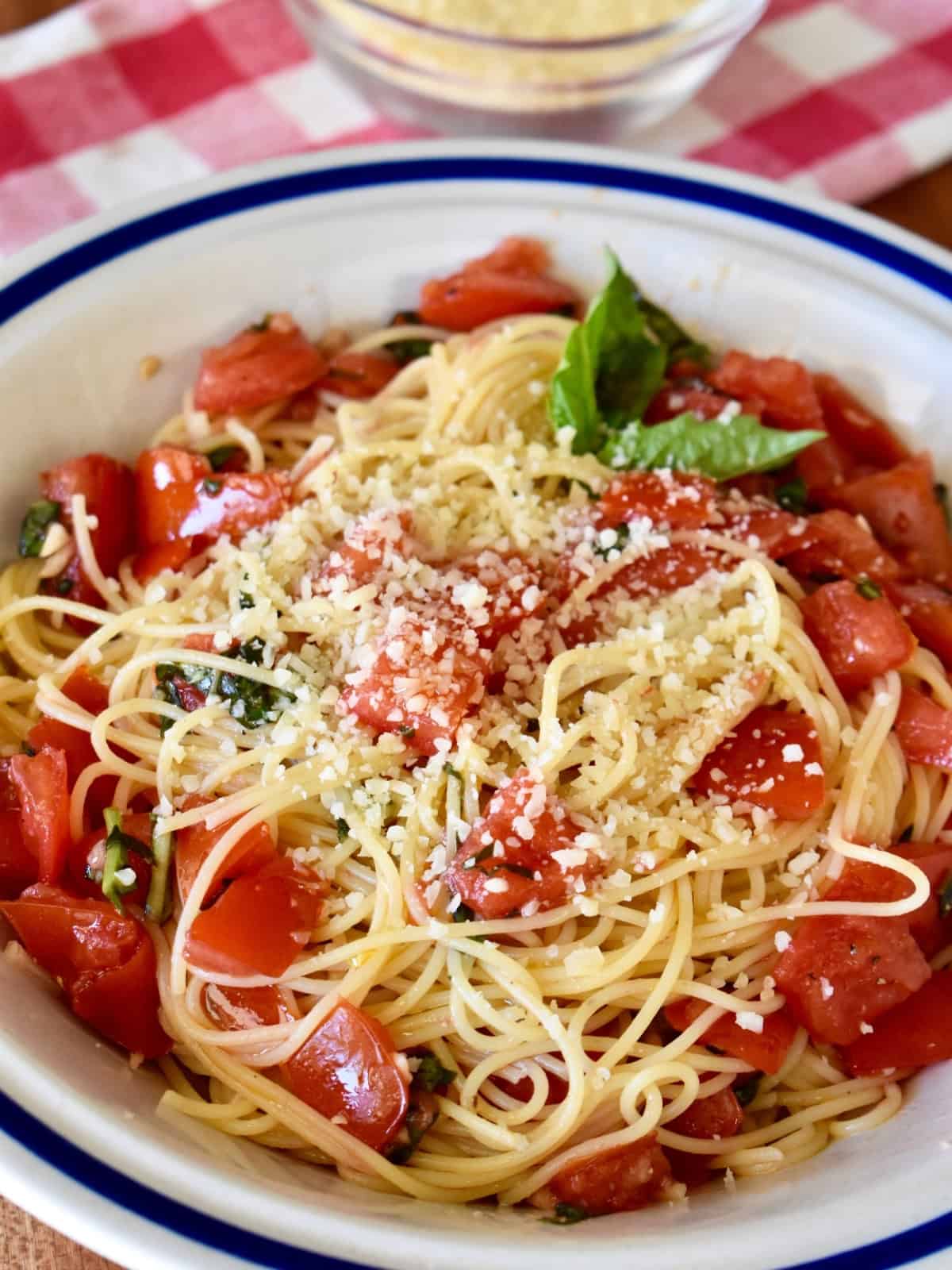 Spaghetti al Pomodoro Crudo in a white bowl with parmesan cheese next to it. 