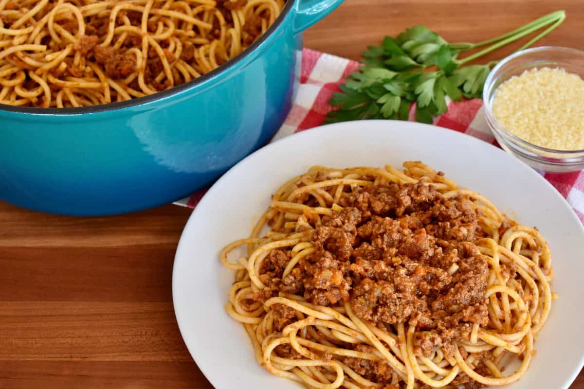 Bolognese sauce tossed with pasta in a white bowl. 