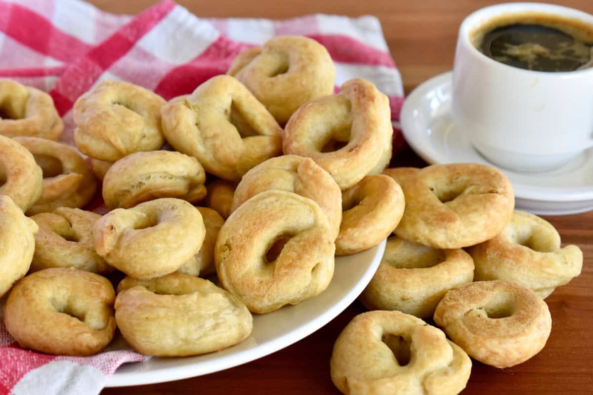Taralli on a white plate with a cup of coffee next to it. 