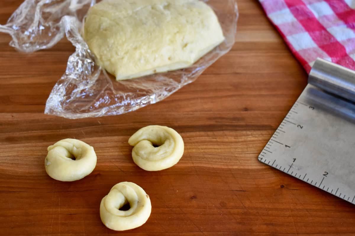 Pieces of dough cut and shaped into ring shapes on a cutting board. 