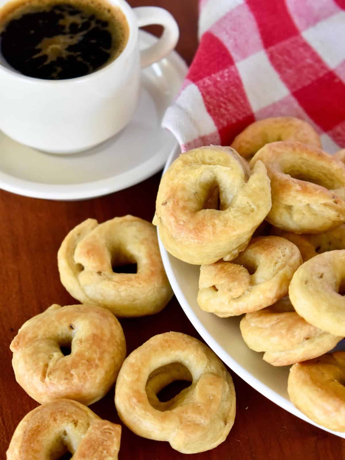Taralli on a white plate with a cup of coffee next to it. 